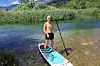 En man på en blå paddlingsbräda i en grund sjö med vass och berg i bakgrunden.
