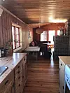 Träpanelklätt rum med långbord, fönster och en murad kamin i en ljus, rustik interiör.