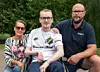 Tre personer utomhus framför en grön häck.