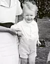 Svartvitt foto av ett litet barn i ljusa kläder som hålls i handen av en vuxen utomhus.