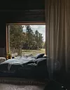 Säng vid öppet fönster med utsikt mot träd och en grön glänta.