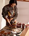 Person dekorerar pepparkakor på plåtar vid ett bord med skålar och bakredskap.