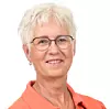 En kvinna med kort blont hår, glasögon och orange skjorta poserar mot vit bakgrund.