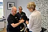Veterinär undersöker en svart och brun hund i ett rum med två andra personer intill.