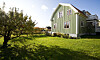 Grönt hus med vita knutar på en solig gräsmatta bredvid träd.