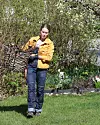 Person i gul jacka bär en korg i en grön trädgård.