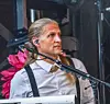 En artist sjunger vid en mikrofon på scenen med keyboard och mörk bakgrund.