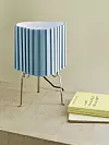 Bordslampa med blåvit veckad skärm står bredvid en gul bok på en beige yta.