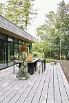 Person går på träterrass intill modernt hus med glasväggar i skogsmiljö.
