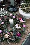 Vinterkrans med ljus, rosa blommor och gröna kvistar på ett bord.
