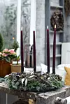 Fyra tända ljus i en grön adventsdekoration på ett gammalt träbord.