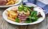 Baconlindad beer can burger på en tallrik med pommes frites, dressing och sallad.