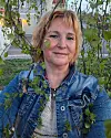 Kvinna i jeansjacka står utomhus under ett träd.