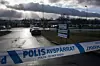 Blåvit polisavspärrning framför en väg med en polisbil och molniga himmel i bakgrunden.