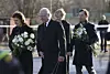 Fyra personer går utomhus med blommor på en väg med polisband i bakgrunden.