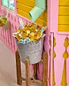 Metallhink med chokladpengar på träpall framför rosa och gul vägg i en butik.