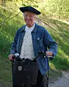 Clownen Manne i blå jacka och svart basker står vid en cykel på en grusväg i naturen.