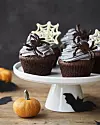 Två cupcakes med frostning och höstdekorationer på ett vitt kakfat bredvid en liten pumpa.