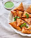 Vitt fat med gyllenbruna triangelformade sambusas och en liten skål med grön dip.