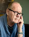 Peter Haber i glasögon och blå tröja sitter och ser eftertänksam ut inomhus.