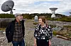 Två personer står på klippor framför stora radioteleskop utomhus.