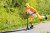 Ett barn i orange djurdräkt åker sparkcykel på en väg bredvid grönska.