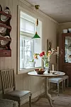 Litet köksbord med blommor och tända ljus framför ett fönster i ett ljust, klassiskt kök.