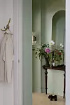 Ljus hall med spegelbord, blomsterarrangemang och en beige rock på en krok.