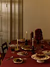 Dukat bord med röda textilier, levande ljus, glas, fat och desserter i ett varmt inrett rum.