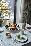 Dukat bord med fruktfat, nötter, koppar och en liten dekoration vid ett fönster med snö utanför.