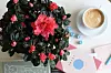 Röd blomsterkrans bredvid en kopp kaffe och kort på ett bord.