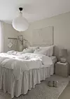 Ljust sovrum med stor säng, beige väggar, taklampa, nattduksbord och fluffig matta.