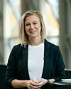 Kvinna i svart blazer och vit topp står framför en ljus glasvägg.