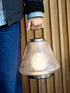 Närbild av en hand som håller en ribbad bordslampa med varmt ljus mot en trävägg.