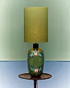 Bordslampa med grön dekorativ fot och gul lampskärm på ett runt sidobord.