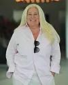 Mia Parnevik i ljusrosa skjorta och ljusa byxor. Hon ler mot kameran och har ett par solglasögon hängandes i skjortan.