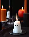 Ett vitt spökformat ljus brinner på en bricka med flera tända ljus i bakgrunden.