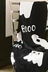 Svartvit textil med spökmotiv och texten ”Booo” draperad över en stol.