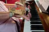 Närbild av händer som spelar piano med hjälp av ”fingerlyftaren”.