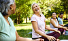 Glad kvinnor sitter på yogamattor i en park.