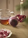 Julstilleben med kopp te, tänt ljus, rosa burk och röda karameller på ett träbord.