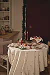 Litet runt bord med tänd ljusstake, frukt, bakverk och juldekorationer i ett rum.
