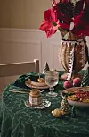 Dukat bord med grönduk, ljus, tallkottar och röd blomsterdekoration vid en vägg.