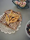 Dekorerat fat med friterade bakverk på en spetsduk, omgiven av skålar med småkakor och bär.