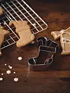 Pepparkakor på galler och metallformar på ett träbord med små vita dekorationer.