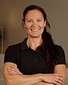 Kvinna i svart tröja står mot neutral bakgrund med armarna i kors och ler mot kameran.