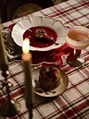 Dukat bord med dessert på tallrik, bröd och levande ljus på rutig duk.