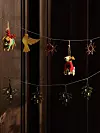 Flera små juldekorationer hänger på snören framför en mörk trävägg.