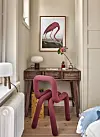 Ett ljust rum med rosa stol, träbord, flamingobild och enkla dekorativa detaljer.