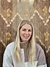 Kvinne i lys, rutete genser foran brun vegg med geometrisk mønster